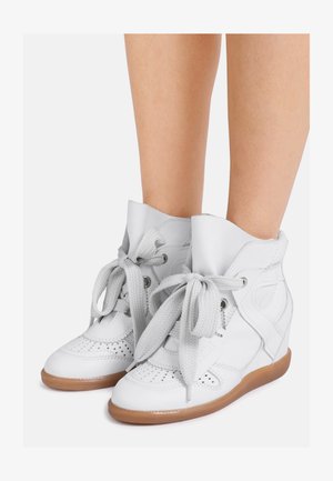 Witte leren wedge sneakers met dikke veters en geperforeerde details, gedragen op blote benen, met lichtbruine rubberen zolen.