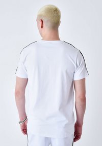 Camiseta blanca de manga corta, con rayas verticales negras en los hombros y una textura suave y ligera.