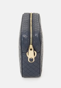 Pochette in pelle intrecciata di colore blu navy con zip dorata, caratterizzata da una texture a motivo diamante e un tirante in metallo.