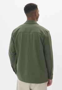 Chemise verte à manches longues avec une texture lisse, dotée d'un col et de poignets à boutons, vue de dos. Design simple et ajusté.