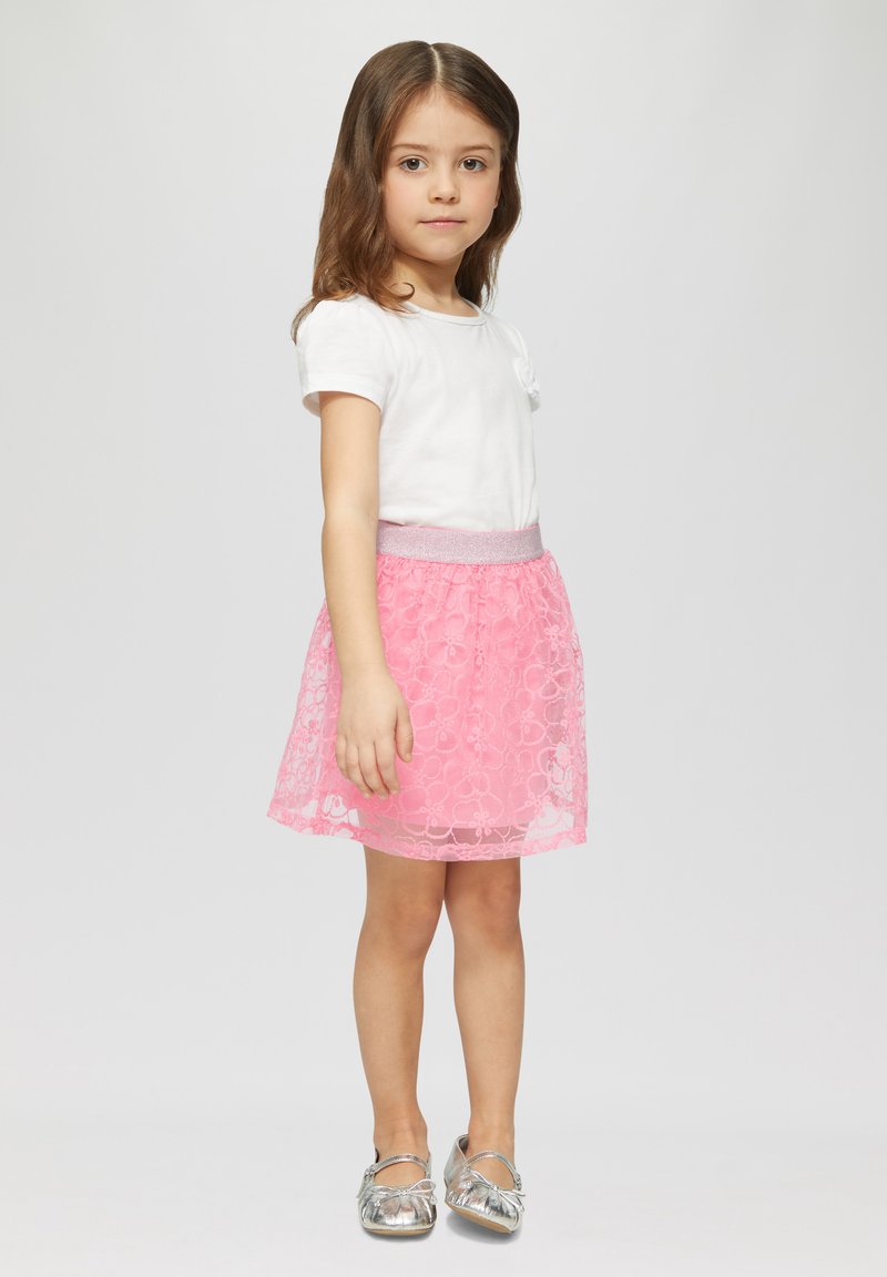 Witte top met korte mouwen, rozenhouten rok met een bloemenpatroon en een zilveren elastische tailleband, gecombineerd met zilveren ballerina's.