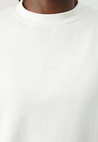 Hvid sweatshirt med ribbet rund hals og subtil tone-i-tone "BORG" broderi på brystet. Blødt, tekstureret stof.