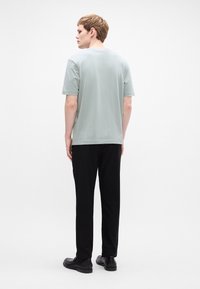 Light grey short-sleeve t-shirt with a rounded neckline, paired with black pants and black shoes, viewed from the back.