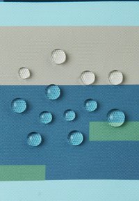 Krople wody o różnorodnych rozmiarach na tkaninie o teksturowanej powierzchni, z poziomymi paskami w odcieniach jasnoniebieskim, beżowym i ciemnoniebieskim z zielonymi akcentami.
