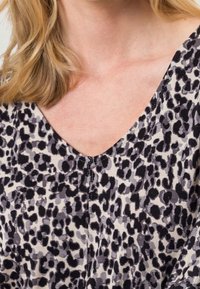 V-Ausschnitt Bluse aus leichtem Stoff mit einem schwarz-grauen Leopardenmuster, sichtbaren Nähten und einer weichen Textur.
