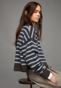 Sweter w paski w odcieniach ciemnobrązowym i jasnoniebieskim, o luźnym kroju, opadających ramionach i prążkowanych mankietach, wykonany z miękkiego materiału.