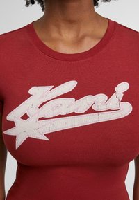 Rode katoenen T-shirt met een ronde halslijn, met een versleten witte graphic van het woord "Kani" en een ster ontwerp op de borst.