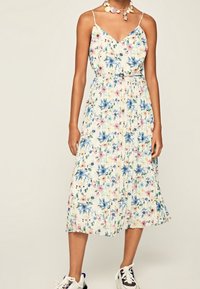 Kwiatowa sukienka maxi na ramiączkach; kremowe tło; z niebieskimi i różowymi kwiatami; ściągnięta w talii; miękka, lejąca tkanina; zestawiona z trampkami.