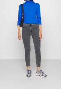 Jersey de cuello alto de rayas azules, jeans gris de cintura alta y zapatillas de running gris con detalles en plata y amarillo. Un bolso negro de hombro añade detalle.