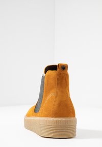 Bottine en suède jaune avec un panneau en tissu gris texturé, une languette ronde à l'arrière et une semelle en caoutchouc avec des rainures verticales.