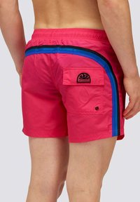 Costume da bagno rosa con strisce laterali blu e nere. Vita elastica, tasca posteriore con logo. Tessuto liscio e leggero.