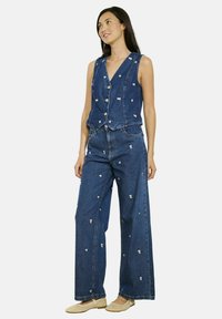 Denima veste un platām biksēm ar baltu ziedu izšuvumu, ar v veida apkakli, pogu aizdari un brīvu piegriezumu. Krāsas ir zila un balta.