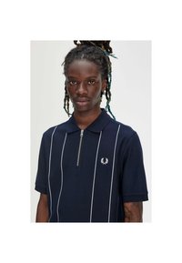 Marineblauwe polo met witte verticale strepen, een halve ritssluiting en een klein logo op de borst. Gemaakt van gestructureerde stof.