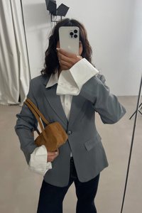 Grå blazer med strukturerede skuldre, parret med en hvid skjorte med overdimensionerede manchetter. Holder en lille brun ruskinds tote.