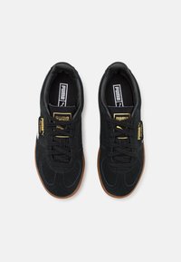 Baskets en suede noir avec une semelle en caoutchouc gomme, dotées de lacets noirs, d'une étiquette logo dorée et d'une doublure intérieure noire ; conçues pour une utilisation décontractée.