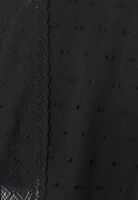 Tessuto nero con superficie testurizzata e piccoli punti in rilievo. Un bordo in pizzo decorativo corre lungo il lato, arricchendo il design complessivo.