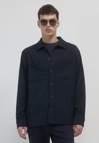 Camicia blu navy con due tasche sul petto e tasche laterali; realizzata in tessuto morbido, con colletto e maniche lunghe.