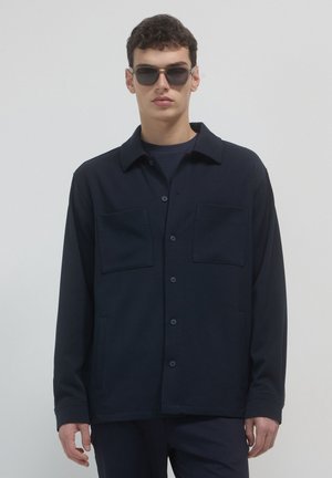 Navy button-up shirt with two chest pockets and side pockets; made of soft fabric, featuring a collar and long sleeves.