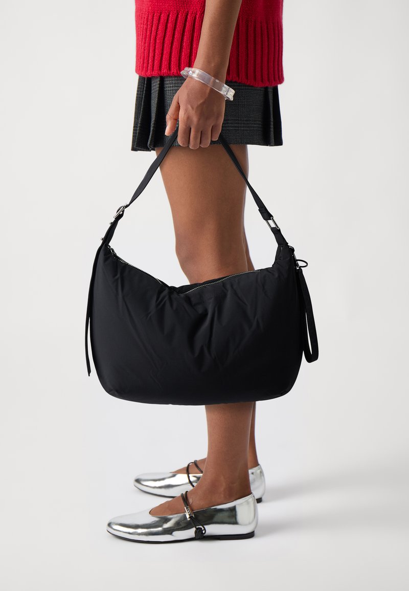 Zwarte nylon schoudertas met een zacht, puffy ontwerp, ritssluiting en verstelbare schouderband. Zilveren platte schoenen met een strakke afwerking en enkelbandje.