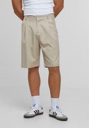 Beige pleated shorts made of lightweight fabric, featuring a button closure and side pockets, paired with white athletic socks and sneakers.