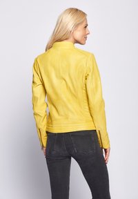 Gele leren jas met een getailleerd ontwerp, voorzien van een hoge kraag en ritsmanchetten. Glad oppervlak met goed zichtbare stiksels.