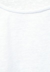 Vit tyg närbild som visar en slät struktur och en rundad halsdesign med en fin stickning, som visar subtila tonvariationer.