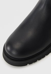 Botte en cuir noir avec un bout arrondi, finition texturée, semelle en caoutchouc et surface supérieure lisse. Pas de matériel ni d'embellissements visibles.