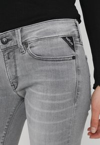 Jeans de mezclilla gris con un diseño clásico de cinco bolsillos, cierre de botón y etiqueta de la marca negra en la cintura para identificación.