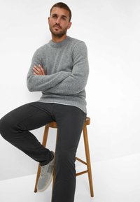 Lichtgrijze gebreide trui met ribbelhals, donkergrijze slim-fit broek en lichtgrijze sneakers op een houten kruk tegen een witte achtergrond.
