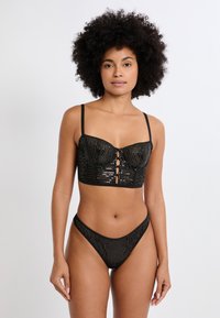 Bralette nera con paillettes a righe verticali, con ferretto di supporto e spalline regolabili, abbinata a un perizoma coordinato con paillettes.