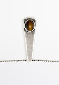 Pendentif en argent de forme triangulaire, présentant une pierre cabochon brune sertie dans un sertissage circulaire et attachée à une chaîne délicate.