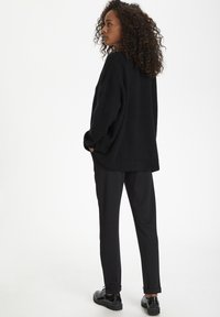 Black oversized sweater made of fluffy material, paired with sleek black trousers and polished black shoes. Simple, textured design.