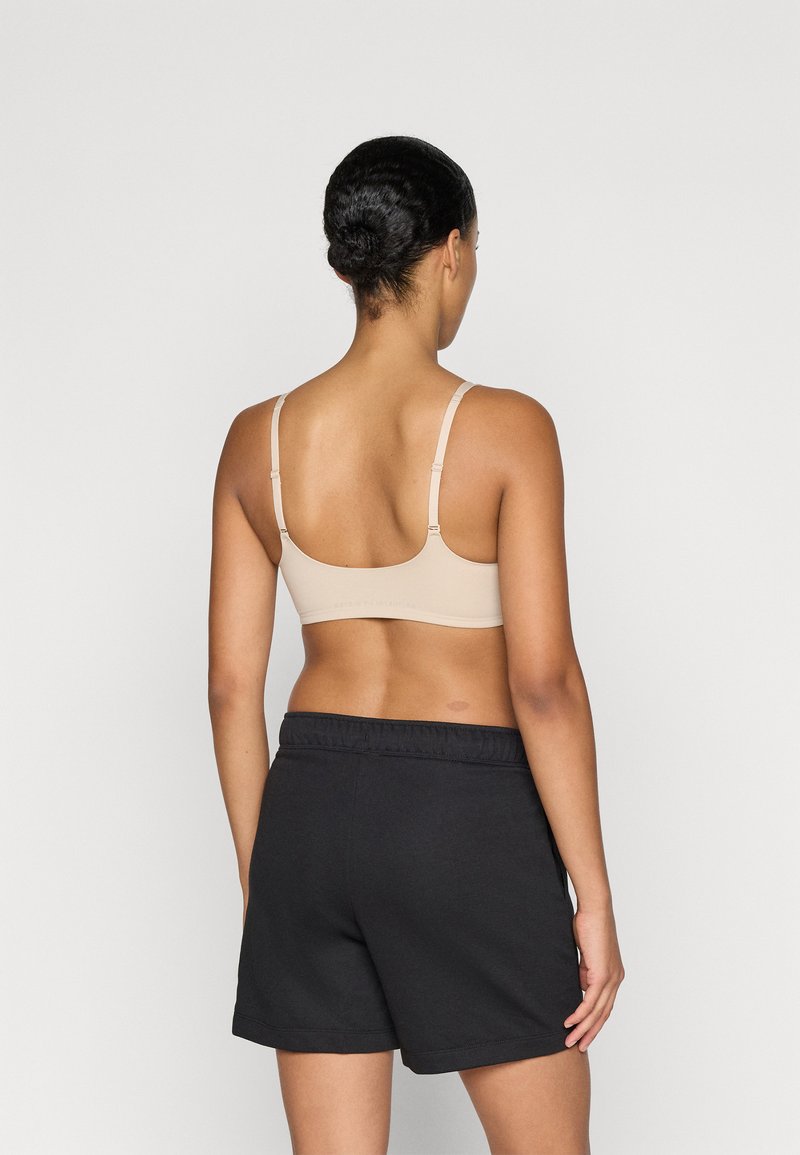 Bralette beige con spalline regolabili abbinata a pantaloni corti neri con vita elastica. Tessuto liscio, design minimalista, senza motivi visibili o hardware.