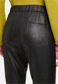 Zwarte nepleer broek met een elastische tailleband, met twee achterzakken en een gestructureerde afwerking. Het materiaal heeft een subtiele glans.