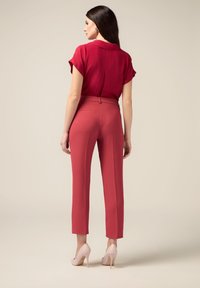Blusa rossa a maniche corte abbinata a pantaloni tailored rosa e tacchi alti rosa chiaro. I pantaloni hanno una vestibilità slim e tasche posteriori.