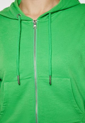 Grüne Zip-Hoodie aus strukturiertem Material, mit Fronttasche und Zugbändern. Verfügt über einen silbernen Reißverschluss und verstärkte Nähte.