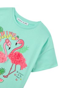 T-shirt verde menta chiaro con due fenicotteri rosa, accentati da texture fluffy, e grafica e testo a tema estivo colorati.