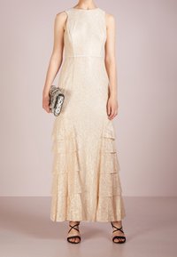 Ecrufärgad spetsklänning med figurnära överdel, utsvängd flerlagerskjol och rund halsringning. Bärs med en mönstrad väska och svarta remsandaler.