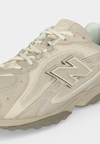 Μπεζ και ανοιχτό γκρι σουέτ και δίχτυ αθλητικό παπούτσι με εκρού κορδόνια και μεγάλο κεντητό λογότυπο "N" στο πλάι.