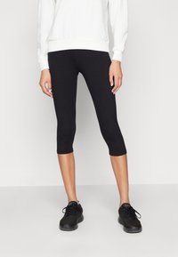 Fekete capri leggings rugalmas anyagból, testhez álló fazonnal, ami éppen a térd alatt végződik, fekete sportcipővel párosítva.