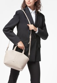 Borsa a mano in pelle beige con forma strutturata, doppi manici e una tracolla staccabile. Presenta una superficie texturizzata e accenti di design triangolari.