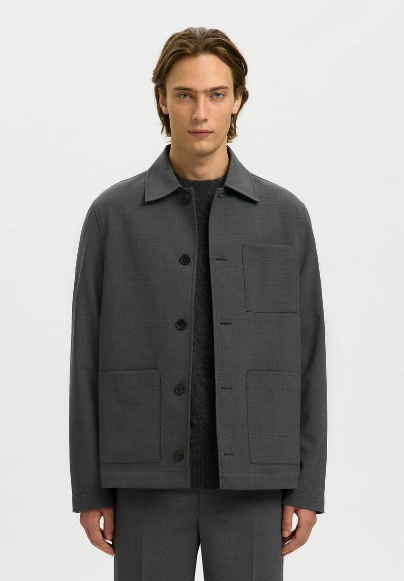 Tumši pelēks žakets ar apkakli, pogu aizdari un divām lielām priekšējām kabatām. Gluda tekstūra ar minimālām šuvju detaļām.