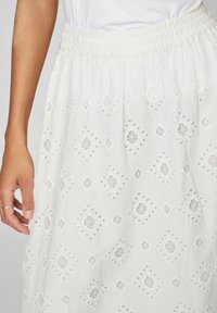 Λευκή κεντημένη φούστα με ελαστική μέση, διακοσμημένη με διαμαντένια και λουλουδάτα σχέδια κομμένα σε ελαφρύ ύφασμα.