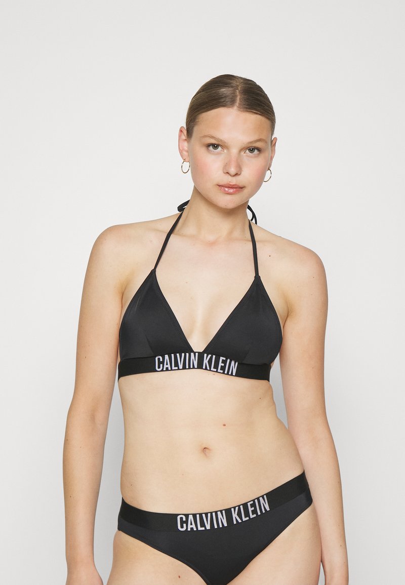Fekete bikini szett háromszög alakú melltartóval és alacsony derekú bugyival, a pántokon fehér "CALVIN KLEIN" felirattal. Sima anyag.