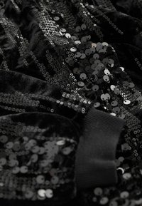 Tissu en velours noir orné de paillettes noires denses cousues en rayures, avec un poignet côtelé probablement provenant d'une manche ou d'un bracelet de vêtement.