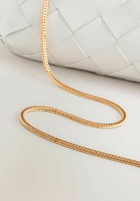 Biała pleciona skórzana torba z paskiem z pozłacanego plecionego łańcucha, spoczywająca na białej powierzchni.