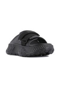 Black sandals with a textured rubber sole, an adjustable Velcro strap, and a molded footbed, featuring a curved design and open toe.