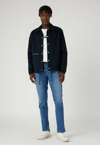 Chaqueta de punto navy con botones a presión, dos bolsillos frontales, dobladillo con cordones, combinada con una camiseta blanca y vaqueros azules, llevada con zapatillas blancas.