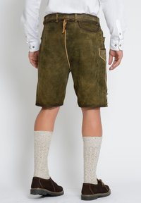 Bruine suède shorts met een gestructureerde afwerking, zijzakken en decoratieve knopen aan de zijkanten, gecombineerd met crèmekleurige gebreide sokken en bruine schoenen.