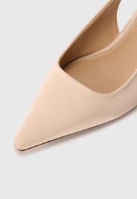 Μπεζ γόβα με μυτερή μύτη, κατασκευασμένη από λείο σατέν υλικό, με σχεδιασμό πλαϊνής κοπής και λεπτή, διαμορφωμένη σιλουέτα.